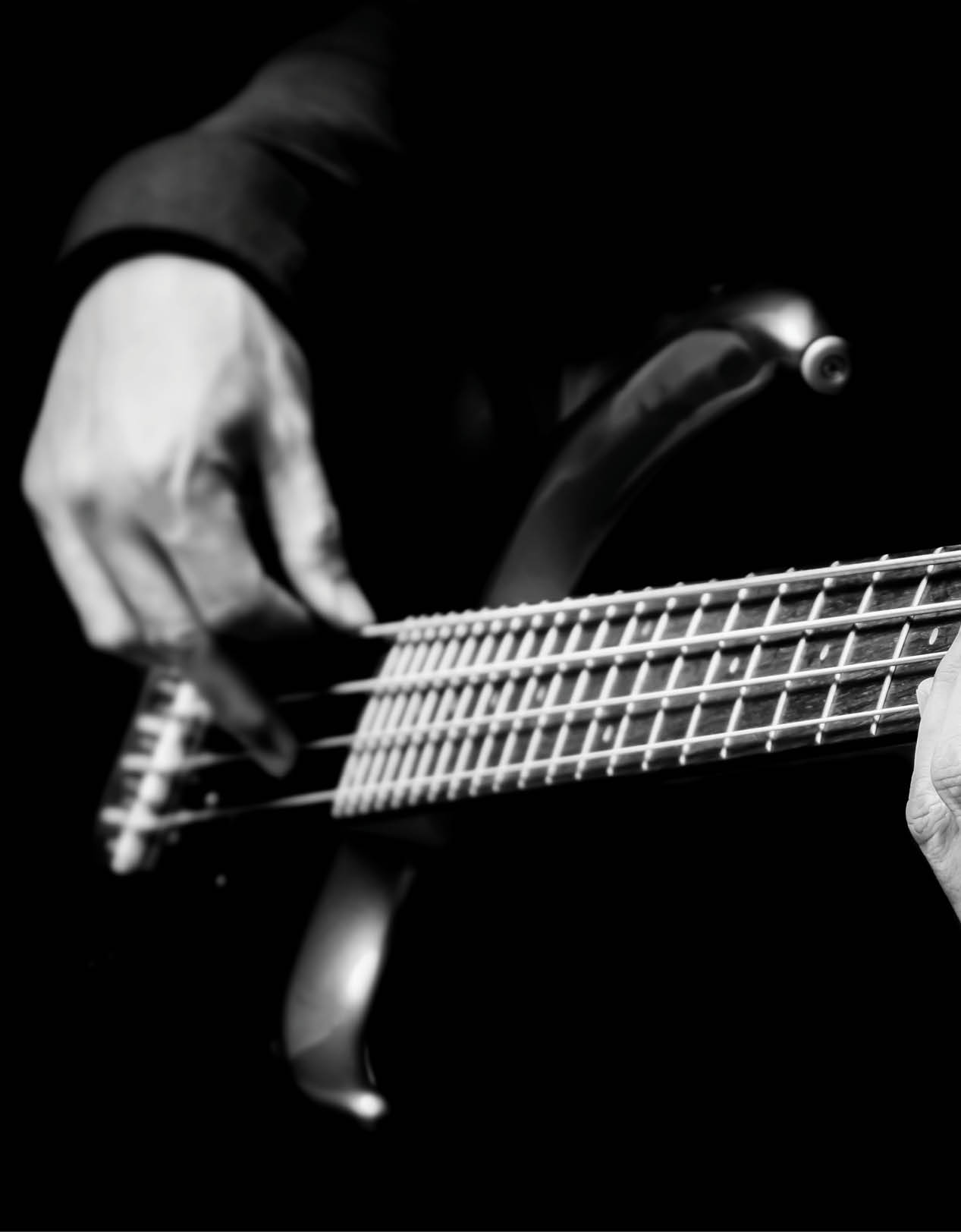 black and white musician hands playing electric bass guitar on black background. music concept